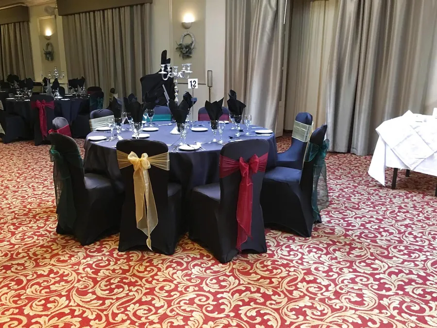 Black stretch chair covers with gold, red and green organza bows around a dinner table